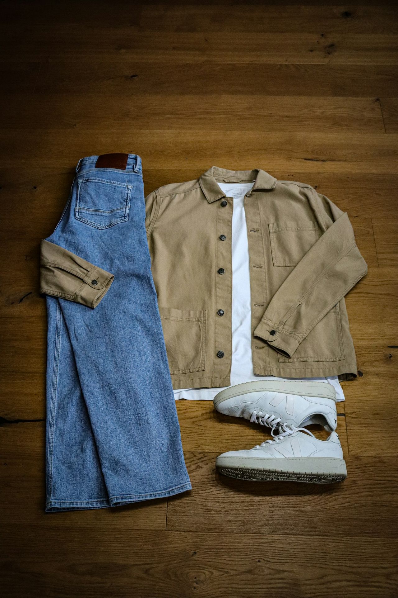 A pair of jeans, a jacket, and a pair of sneakers are laid out